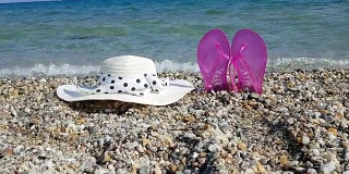 粉色人字拖和沙砾沙滩上的帽子