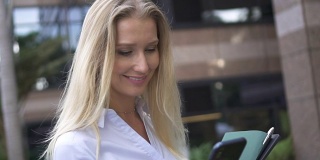 一名职业女性员工站在一栋办公楼前低头看手中的智能手机