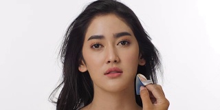 近距离拍摄有吸引力的亚洲女人从专业化妆师化妆。在纯白背景下使用海绵粉底。美丽和时尚的概念。