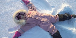在一个寒冷晴朗的日子里，小女孩躺在雪地里做了一个雪天使