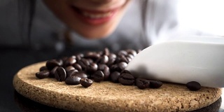 年轻的咖啡师闻着桌上的咖啡豆，脸上挂着笑脸