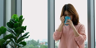 年轻美丽的亚洲女人喝咖啡，透过窗户与城市的看法与幸福，人们的生活方式