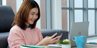 年轻美丽的亚洲女人使用智能手机与幸福，而工作与笔记本电脑，人们在电话上，生活方式，在家里工作