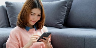 年轻美丽的亚洲女人用智能手机与幸福坐在客厅，人们在电话，生活方式