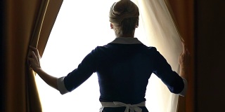 豪华酒店的女服务员穿着最好的西装拉开窗帘，准备打扫房间