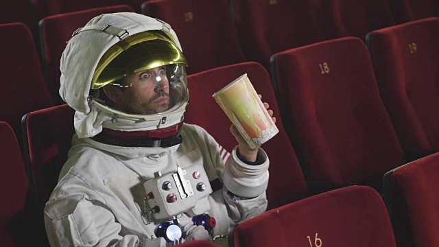 一名宇航员一边看电影一边吃着爆米花，享受着电影的乐趣。概念:电影和太空电影，电影的另一个世界，超现实的情况。