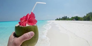 个人观点:马尔代夫阳光明媚的热带海滩上，男人喝着椰子饮料