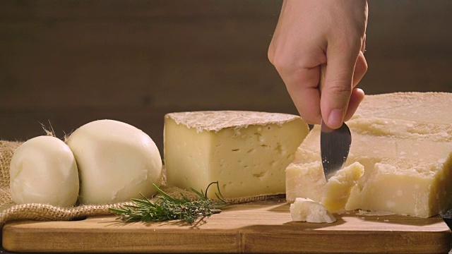 帕尔玛干酪的混合物，放在木砧板上。一只手拿着刀，掰开几块来品尝质量。