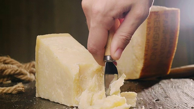 帕尔玛干酪的混合物，放在木砧板上。一只手拿着刀，掰开几块来品尝质量。