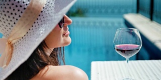 肖像微笑的漂亮女人在松软的帽子和太阳镜享受日光浴与酒杯的葡萄酒