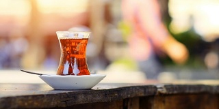 路边茶馆的桌子上放着一杯特制的土耳其茶，背景上是一些模糊的人