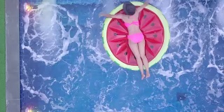 俯视图的一个女人在比基尼上漂浮的独角兽橡胶。在酒店或度假村享受游泳池的休闲时光