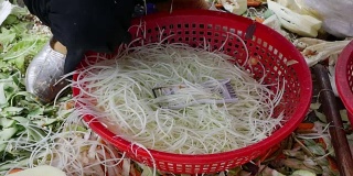 在当地市场，一名妇女将青木木瓜切成丝，放在篮子里做沙拉。特写镜头