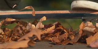 慢镜头:一个不认识的人滑过一堆五颜六色的秋叶。
