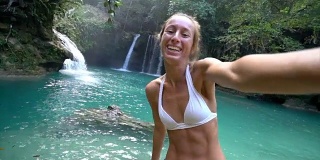 一名年轻女子在菲律宾宿务岛与美丽的瀑布自拍。人们旅游自然自拍的概念。一个人只喜欢户外和一个宁静的环境-慢动作视频