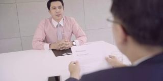慢镜头——迷人的年轻亚洲商人在面试中与正在看他简历的公司人事经理。一名亚洲商人正在面试一名男性求职者。
