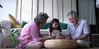 一对老人和孩子一起在家里的客厅玩拼图游戏。白种人的家庭观念，教育，成长学习和发展的年龄。4 k决议。