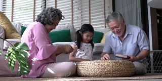 一对老人和孩子一起在家里的客厅玩拼图游戏。白种人的家庭观念，教育，成长学习和发展的年龄。4 k决议。