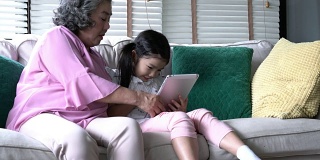 老女人和孩子们一起坐在家里的客厅里，拿着平板电脑。家庭观念、教育技术、成长学习、心理健康与年龄发展。4 k决议。