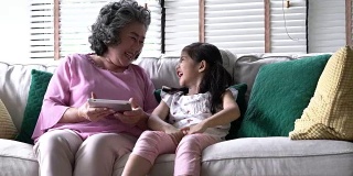 老女人和孩子们一起坐在家里的客厅里，拿着平板电脑。家庭观念、教育技术、成长学习、心理健康与年龄发展。4 k决议。