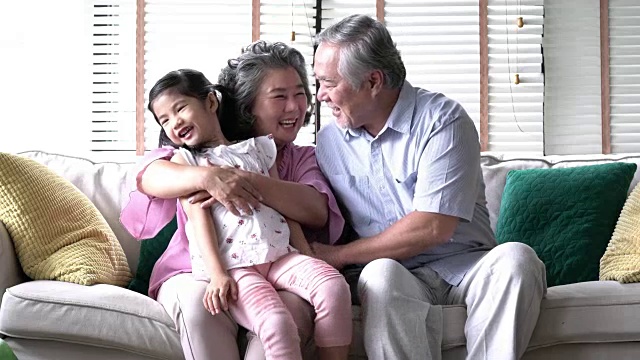一对老夫妇抱着孩子一起坐在家里客厅的大腿上。幸福家庭、优质生活、心理健康、积极心理。4 k决议。
