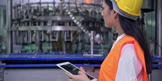 在工厂工作的女工业工程师。年轻漂亮的中国工程师在大型工厂工作。戴安全帽，穿安全服。以高科技自动化机器为背景。