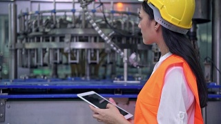 在工厂工作的女工业工程师。年轻漂亮的中国工程师在大型工厂工作。戴安全帽，穿安全服。以高科技自动化机器为背景。视频素材模板下载