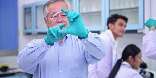 科学家们在实验室里工作。高级中国男性科学家工作在实验室肖像和他的团队在背景。