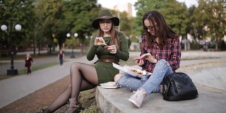 在公园里野餐。两个时髦女孩一边聊天一边吃三明治。这个节日三明治。