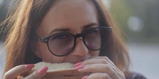 一个女孩正在享用一个新鲜的三明治。戴眼镜的女孩吃三明治吃快餐