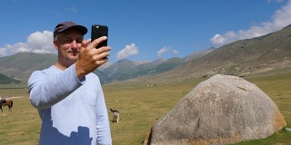 男游客在草地上的大石头附近用手机自拍拍摄视频