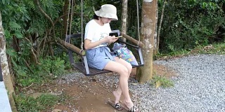 4k亚洲女性使用智能手机，坐在秋千上
