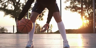 一个女性运动员的腿在白色高尔夫球袜和运动鞋的近镜头。女篮球运动员用手来回弹跳球。阳光照在背景上