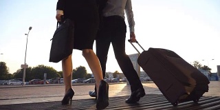 商务人员带着行李通过自动玻璃门离开机场。穿着高跟鞋的年轻男女从航站楼走出来，用轮子推着行李箱。出差的概念。慢动作低角度视角特写