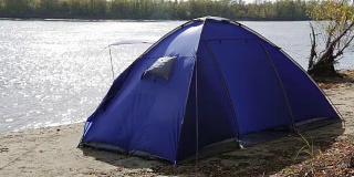 秋天的河边，一个孤独的蓝色帐篷被一阵大风吹起