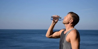 一名男子一边喝水，一边把塑料瓶里的水倒在海里，让自己在锻炼后神清气爽