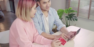一对年轻的亚洲家庭夫妇周末一起坐在家里的桌子上，用平板电脑讨论新闻或网购，认真的男人和女人浏览网页寻找新的优惠。
