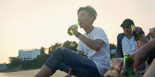 年轻的亚洲成年人悠闲地坐在海滩上喝啤酒