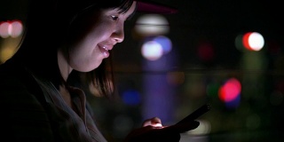 年轻的亚洲女人在新加坡城市的晚上用手机发短信