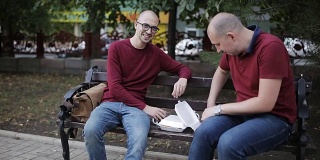 男人们坐在公园的长椅上吃着三明治和薯条，用杯子喝着咖啡聊天