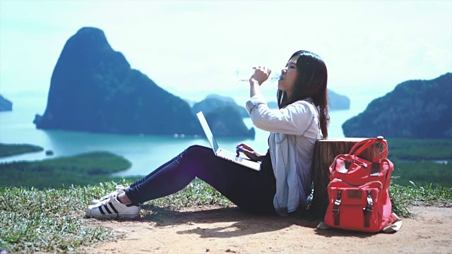 迷人的亚洲女性旅行者在山顶上工作和饮水看风景，感受自由和享受自然的4K慢镜头在samenang Chee，旅行和幸福的生活理念