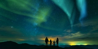 一家人站在岩石上，以北极光为背景。时间流逝