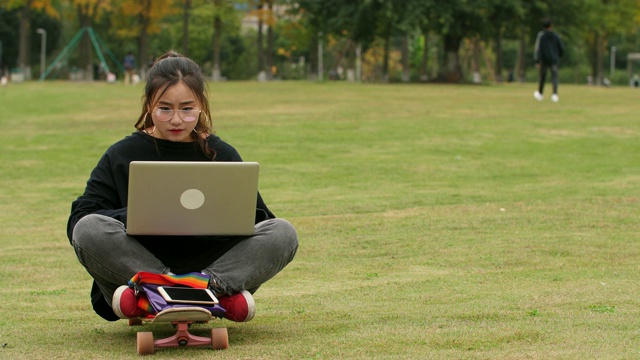 一个亚洲女大学生在校园里的草坪上用笔记本电脑