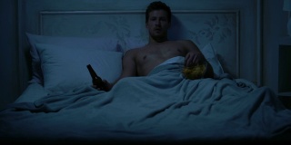单身男性躺在床上，看电视，吃零食，慵懒的周末