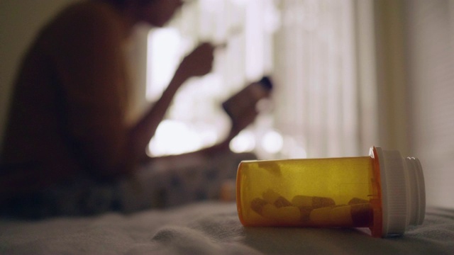 年轻的亚洲女人拿着药瓶，在卧室里讲手机