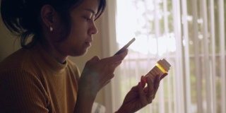 年轻的亚洲女人拿着药瓶，在卧室里讲手机