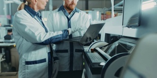 在高科技工厂女性和男性工程师交谈和使用计算机编程的拾取和放置电子机械的印刷线路板表面安装装配线。使用SMT设备生产PCB。
