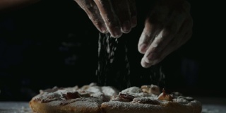 在慢镜头中，女人用手往披萨上撒面粉