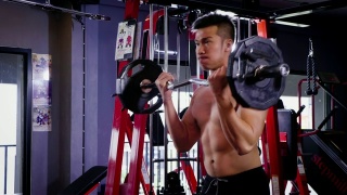年轻的健身男子做二头肌卷曲与E-Z酒吧在健身房，健身训练的概念视频素材模板下载