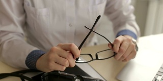 一个女人医生拿着她的眼镜坐在一张桌子在医院里的特写
